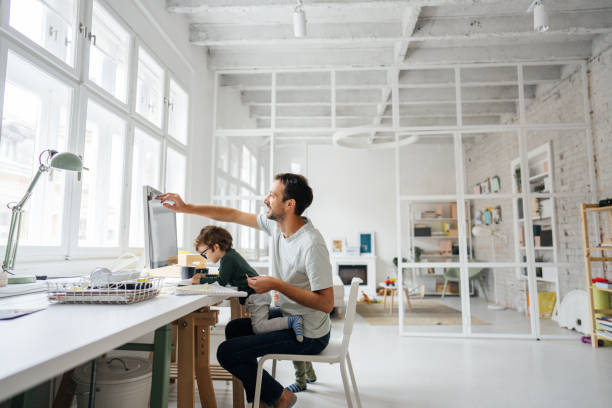Working dad Photo of a young working father and his son spending time together in his home-based office; the daily routine of a modern single father. young graphic designer stock pictures, royalty-free photos & images