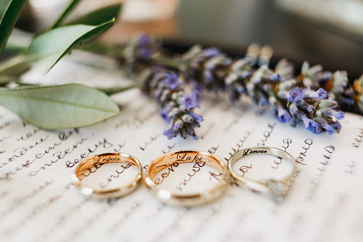 Primer plano de anillos de boda de la novia y el novio y anillos de oro blanco con inscripciones en un pedazo de papel con un juramento y una ramita de lavanda. photo