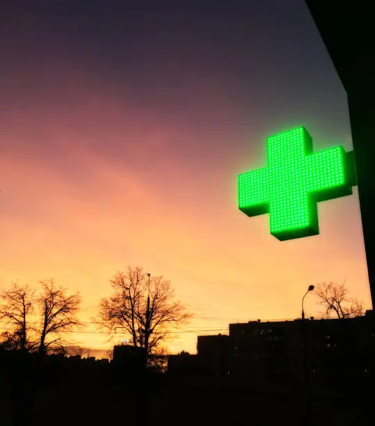 Photo of A green led pharmacy sign in front of a sunset