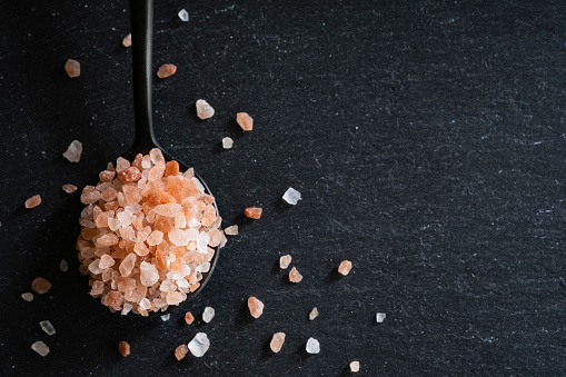 Pink Himalayan salt in a spoon on slate with copy space.