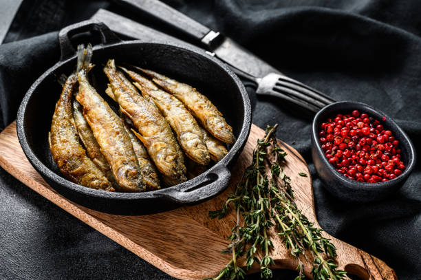 istock Fried smelt in the pan on the table with tomatoes and pepper. Black background. Top view. 1267737462