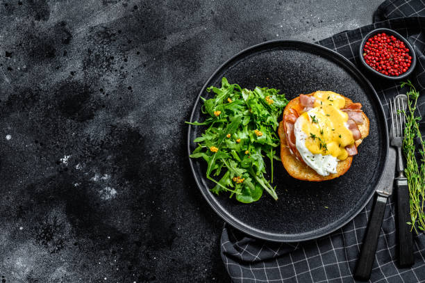 Breakfast Burger with bacon, egg Benedict, hollandaise sauce on brioche bun. Black background. Top view. Copy space