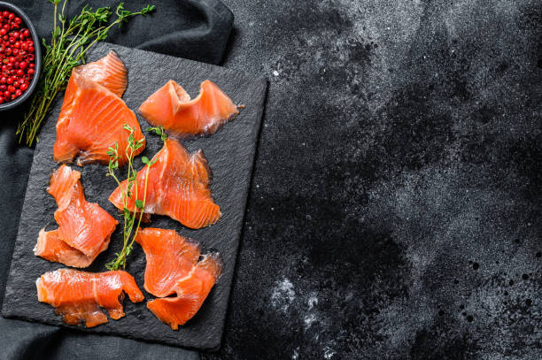 istock Salted salmon slices with pepper and thyme. Organic fish. Black background. Top view. Copy space 1267738512