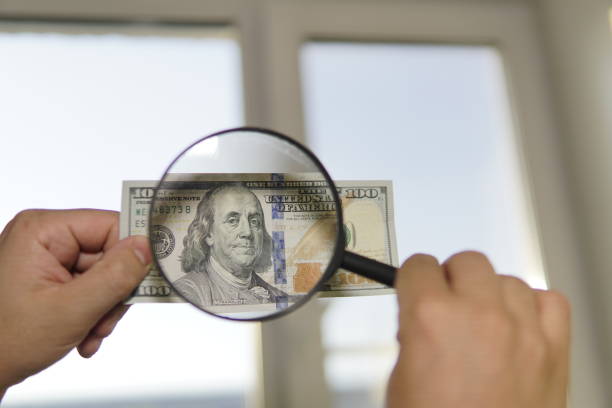 istock Checking counterfeit money light. 100 dollars against the window in his hand. Check for watermark on new hundred dollar bill. translucence of American currency. 1267747911
