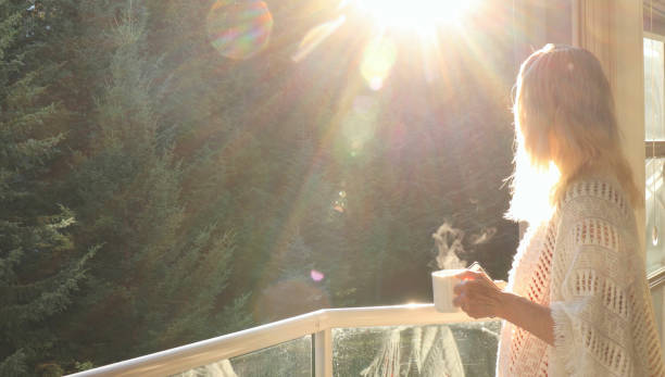 She holds cup of steaming beverage. Forest in distance