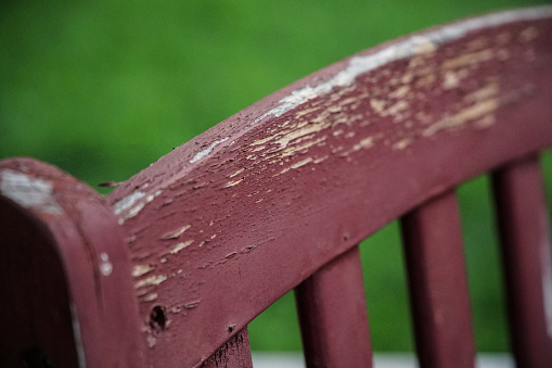 Maroon chair in backyard weathered from the sun. Shallow depth of field focus on the peeling paint.