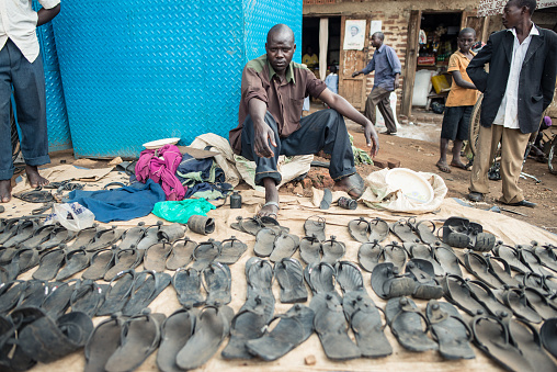 Fort Portal / Uganda - September 30, 2016: Portrait of seller in stall selling sandals made from used tires at a market in countryside Uganda