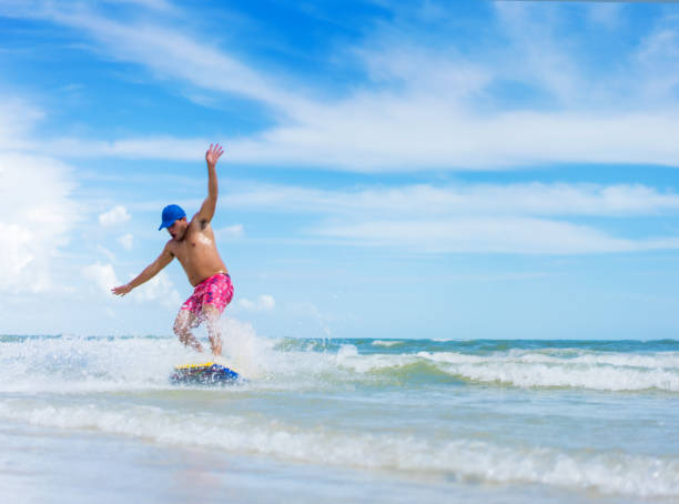 молодой испаноязычный человек на обезжиренной доске - skimboard стоковые фото и изображения