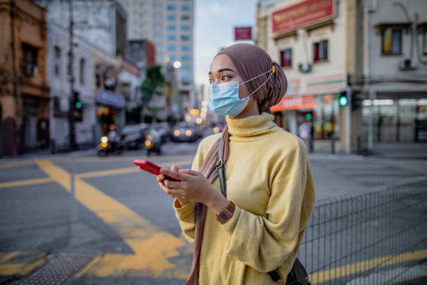 Young asian girl using phone Young asian girl using phone at street and she is wearing brown hijab with yellow shirt. She is waiting for friend or uber or grab at road side. modest clothing stock pictures, royalty-free photos & images