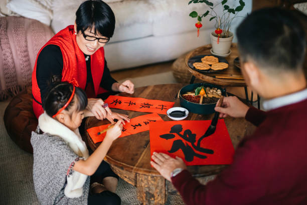 großeltern üben chinesische kalligraphie für chinesisches neujahr fai chun (ausserliche botschaften) und lehren ihre enkelin, indem sie es auf couplets zu hause schreiben - chinese script text calligraphy grandmother stock-fotos und bilder