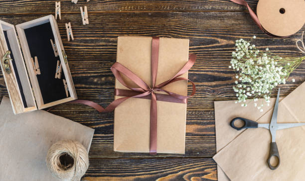 istock Craft paper and tools for creating and decorating gift packaging. There is cardboard, brown ribbons and rope on a wooden table. Concept of a creative approach to creating gift packaging with handmade. 1267808312