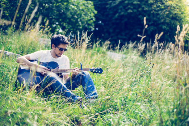 istock Making music outdoors: Young man plays the guitar at a river, summertime 1267821032