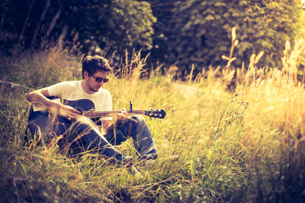 istock Making music outdoors: Young man plays the guitar at a river, summertime 1267821237