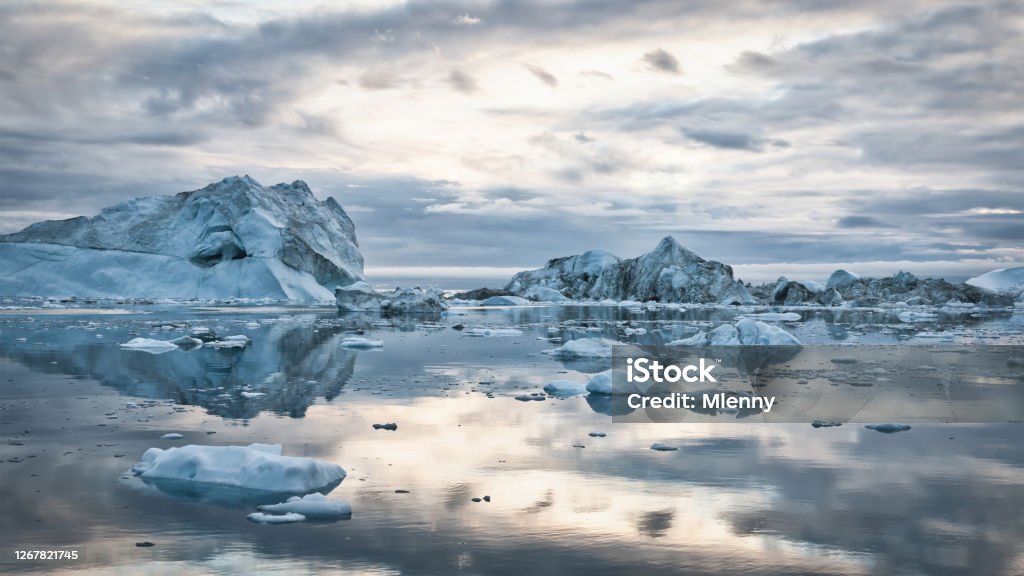 Greenland Icebergs Sunset Cloudscape Panorama Greenland Arctic Icebergs Sunset Twilight Panorama. Large arctic Iceberg drifting on the polar waters under moody sunset skyscape, cloudscape mirroring in the calm water. Arctic Ocean, Illulissat, Greenland, Denmark, North Polar Region Arctic Stock Photo