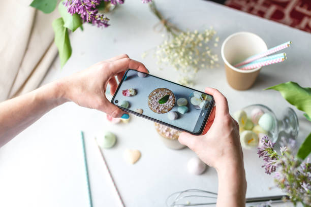 Photo of A woman is taking photos on a mobile phone camera of a whipped morning Dalgona coffee. White background, pastel colors and lilac flowers