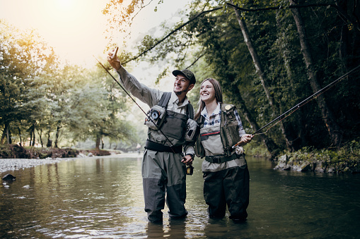 Young adult couple is fishing together on fast mountain river. Active people and sport fly fishing concept.