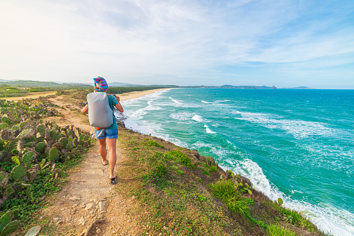Woman with backpack looking at tropical coast from cliff above. Vietnam travel destination, Phu Yen province between Da Nang and Nha Trang. Gorgeous golden sand beach blue waving sea