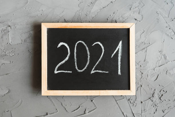 istock New Year 2021. Handwritten text on small blackboard with wooden frame, concrete wall as background, overhead view 1267831492