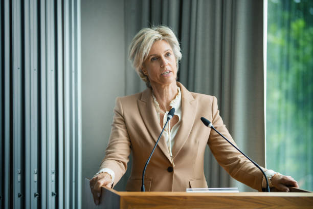 Management staff speaking at a company meeting Closeup front view of an early 50’s company executive having a public addressing in a board room. She’s talking about recovery strategy after coronavirus economy collapse. woman press conference stock pictures, royalty-free photos & images