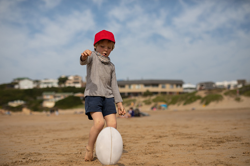 A young boy is kicking a rugby ball on the beach. He is practicing his place kicks. The beach is close to Knysna, South Africa