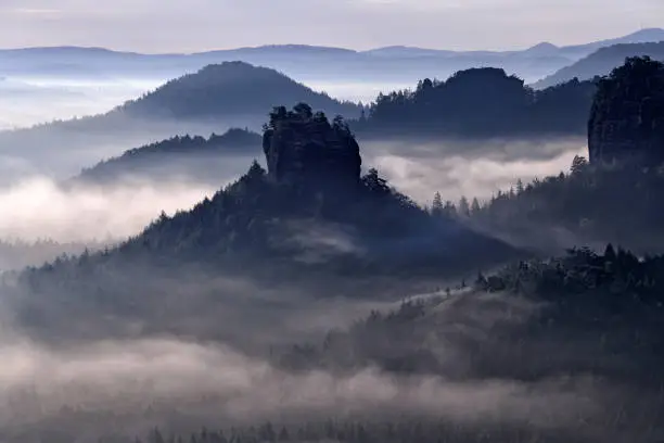 Photo of Kleiner Winterberg, beautiful morning view over sandstone cliff into deep misty valley in Saxony Switzerland, landscape in Germany. Fog and beautiful backlight. Stone hill sunset. Rocky landscape in Europe.