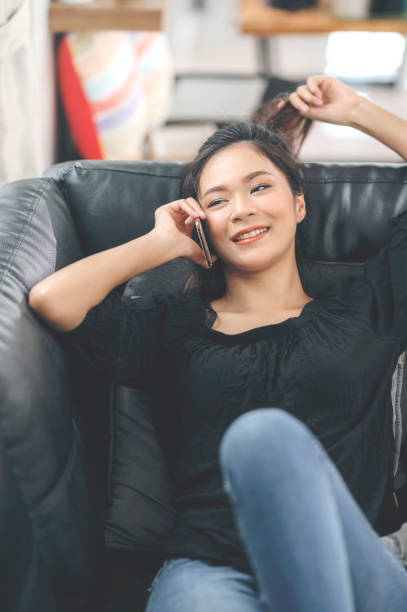istock Happy young asian woman using mobile phone while sitting a couch at home. 1267859821