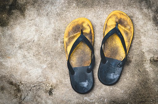 Old and shabby yellow flip-flops lay on the concrete floor.