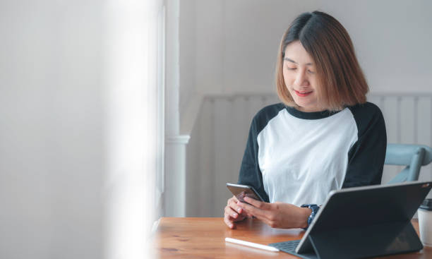 istock Young asian woman using smartphone and laptop working at home. 1267863687
