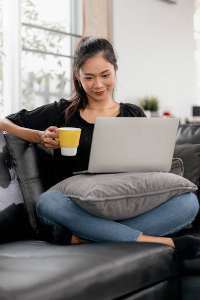 istock Young asian woman using laptop while sitting on a couch at home. 1267868832