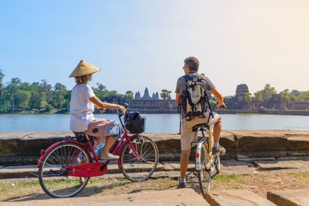 pareja turística en bicicleta en el templo de angkor, camboya. fachada principal de angkor wat reflejada en el estanque de agua. turismo ecológico viajando. - cambodia khmer architecture outdoors fotografías e imágenes de stock