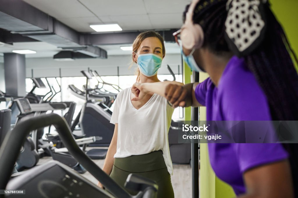 Two Women Greeting With Elbow Bump In The Gym During Coronavirus Pandemic Two woman with protective face mask greeting with elbow bump in the gym during coronavirus pandemic. 20-24 Years Stock Photo