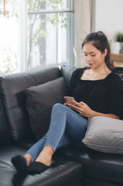 istock Happy young asian woman using mobile phone while sitting a couch at home. 1267906114