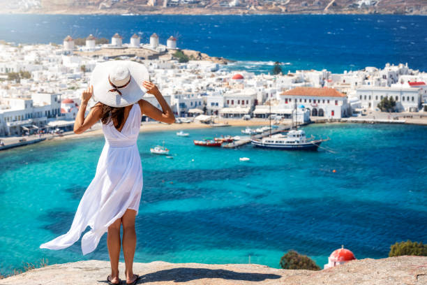 A woman in a white dress enjoys the view to Mykonos, Greece A beautiful traveler woman in a white summer dress enjoys the view to Mykonos island, Cyclades, Greece mykonos photos stock pictures, royalty-free photos & images