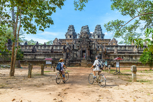 Tourist couple cycling around Angkor temple, Cambodia. Ta Keo building ruins in the jungle. Eco friendly tourism traveling.