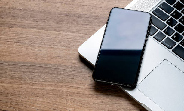 istock Mockup smartphone with blank screen with laptop on wooden table, copy space, top view. 1267927341