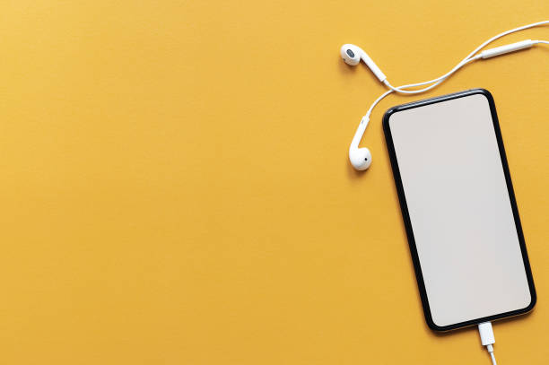 istock Top view blank screen smartphone with headset on yellow leather top table, copy space. 1267928589