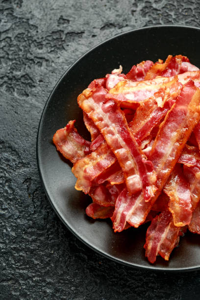 обжаренные хрустящие кусочки streaky bacon в черной тарелке - ham strips стоковые фото и изображения