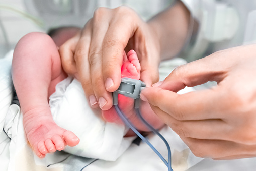 Nurse is putting on the foot of neonatal premature infant pulse oximeter for premature babies, selective focus. Newborn is placed in the incubator. Neonatal intensive care unit