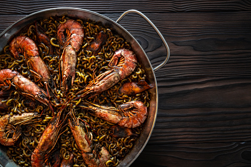 Fidegua pasta paella recipe in a pan with shrimp squid and seafood a Mediterranean food Spain on dark wood