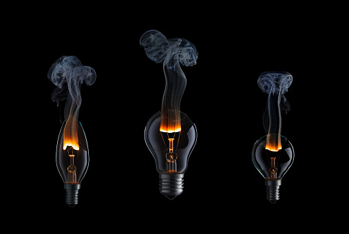 Collection of light bulbs with fire and smoke on black background.