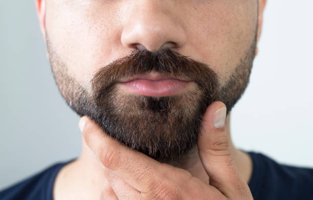 primo piano di giovane barbuto che si tocca la barba mentre si trova su sfondo grigio - one man only human age mustache beard foto e immagini stock