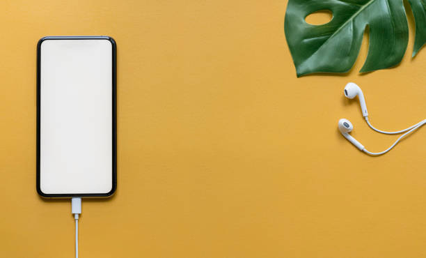 istock Mockup blank screen smartphone with earphone on yellow leather top table, copy space. 1267940116