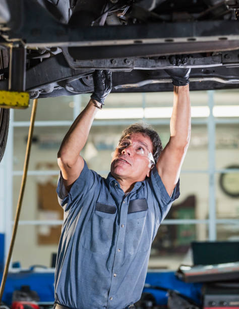 Senior Hispanic man working in auto repair shop A senior Hispanic man in his 60s in an auto repair shop, a mechanic working on the undercarriage of a car. mechanic working under car stock pictures, royalty-free photos & images