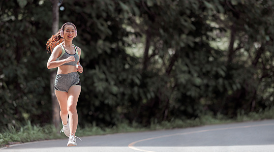 Young beautiful asian woman in sportswear and headset running outdoors on the road with happiness.