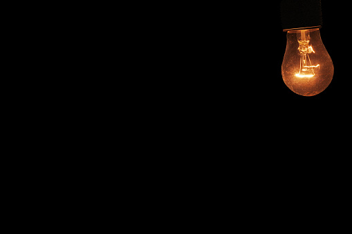 burning light bulb on black background with free space for text