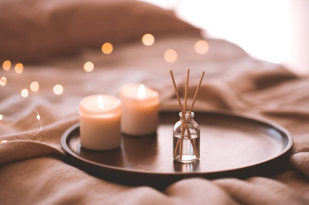 Cozy atmosphere indoors Aroma bamboo sticks in bottle with scented liquid with candles staying on wooden tray in bed closeup. hygge photos stock pictures, royalty-free photos & images
