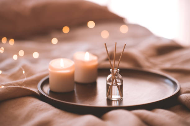 Cozy atmosphere indoors Aroma bamboo sticks in bottle with scented liquid with candles staying on wooden tray in bed closeup. home diffuser stock pictures, royalty-free photos & images