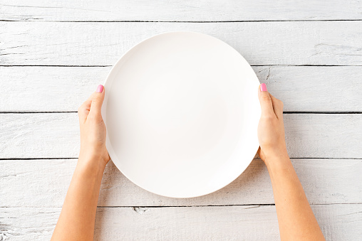 Overhead shot of female hands holding empty white plate over wooden background. Close up