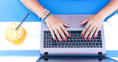 Female hands typing on laptop during smart working outdoors - Modern laptop on the turquoise wooden desk - Orange juice in a retro glass jar for healthy drink break - Remote working concept - Top view