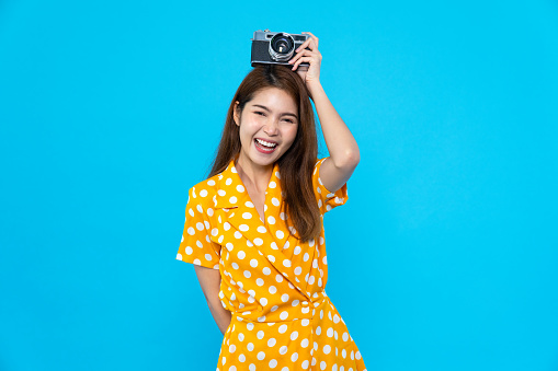 Portrait of cute Asian woman smiling, holding retro camera with funny pose. Happy people, colorful summer fashion, or travel lifestyle concept